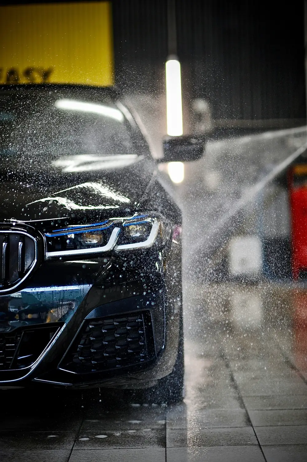 Schwarzes Auto wird in einer Waschanlage abgespritzt